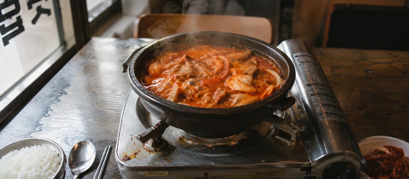 Budae jjigae army stew bubbling in a shallow pot with Spam, sausage, ramyeon and kimchi