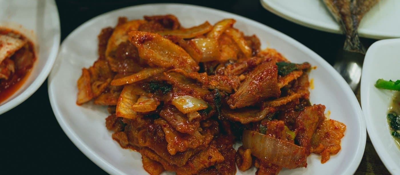 Stir-fried kimchi glossy with gochujang on a white plate, surrounded by small banchan dishes