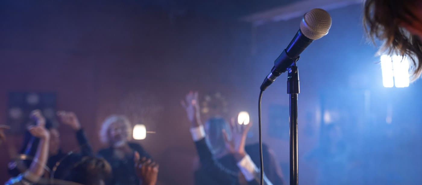 A microphone on a stage washed in blue light, with a blurred crowd behind it