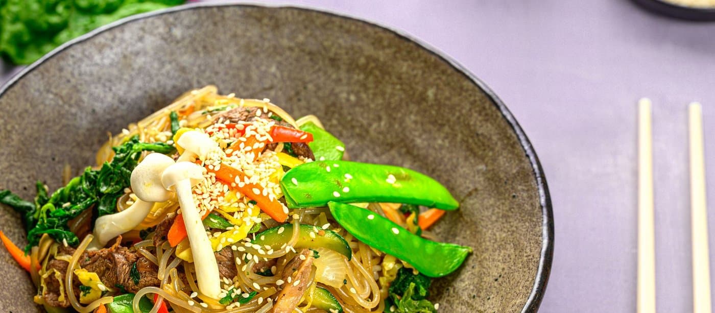 Japchae — glass noodles tossed with beef, mushrooms, snow peas and carrot in a stone bowl