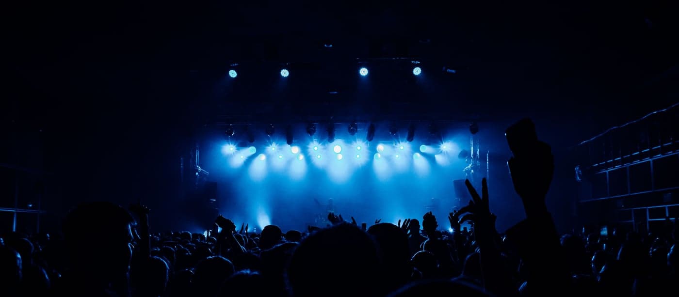 A concert crowd in silhouette facing a stage washed in blue light before a K-pop comeback show