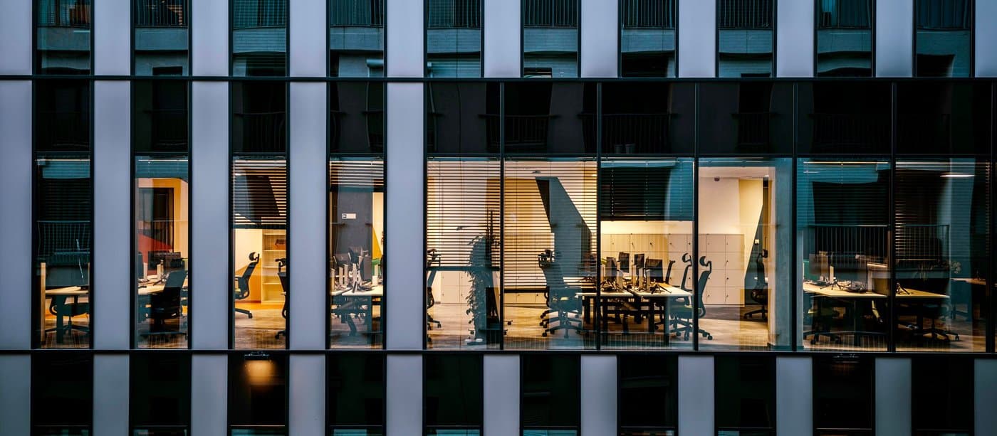 Office floors lit at night behind the vertical fins of a glass tower
